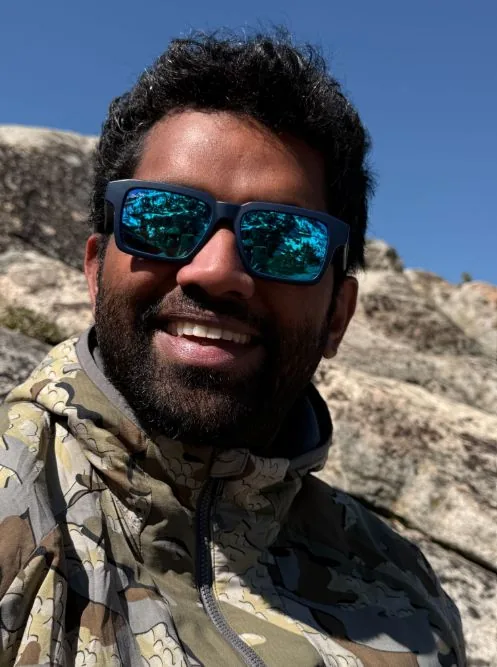 Dilip Ramachandran outdoors on a rocky slope in sunglasses and a hooded jacket